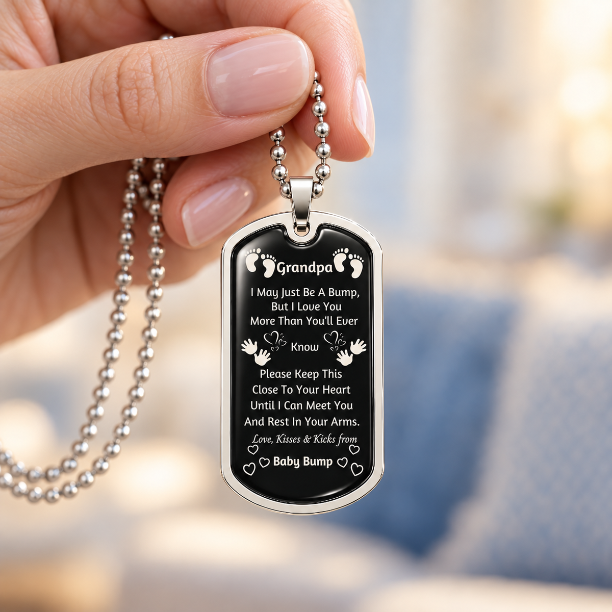 Woman’s hand holding a silver-tone Grandpa baby bump dog-tag necklace with a loving message from an unborn grandchild.