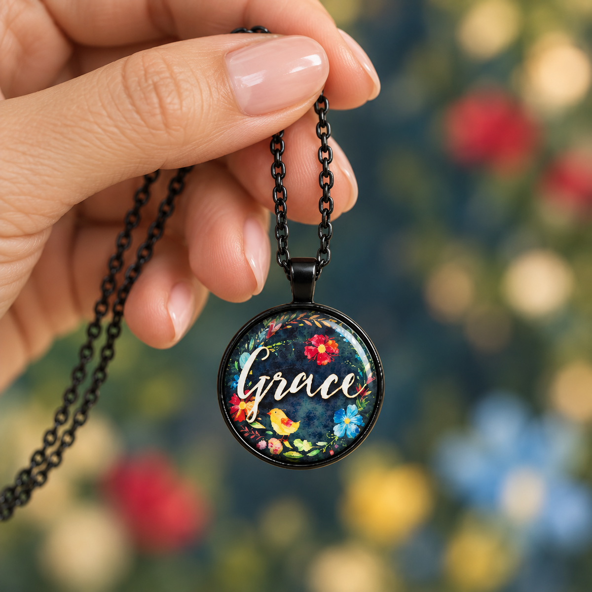 Woman’s hand holding a black round Grace necklace with colorful floral artwork and gold script lettering.