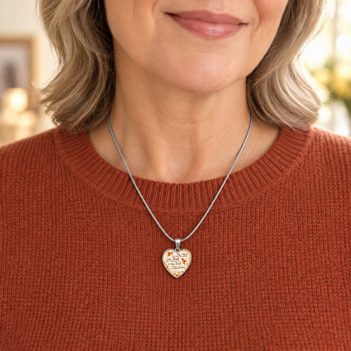 woman in orange sweater wearing Heart-shaped hummingbird memorial necklace with orange floral details and the message “My soul knows you are at peace.”