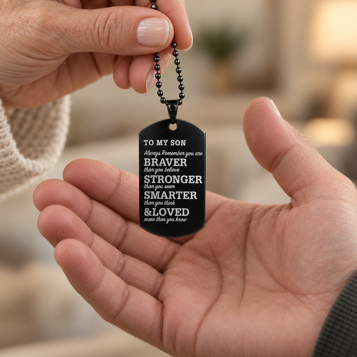 Black To My Son dog tag necklace being passed from a mother to her adult son, showing its tall, narrow proportions and realistic size.