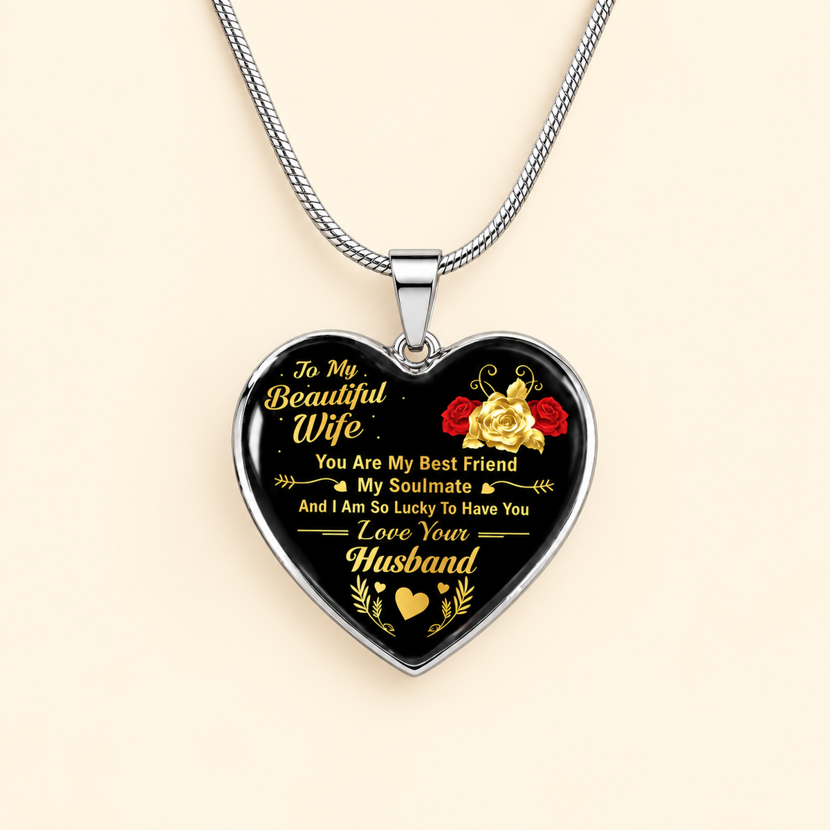 A heart-shaped pendant necklace with a black background and silver-toned metal border, featuring gold and red text and floral graphics. The pendant hangs from a silver chain against a light beige background.