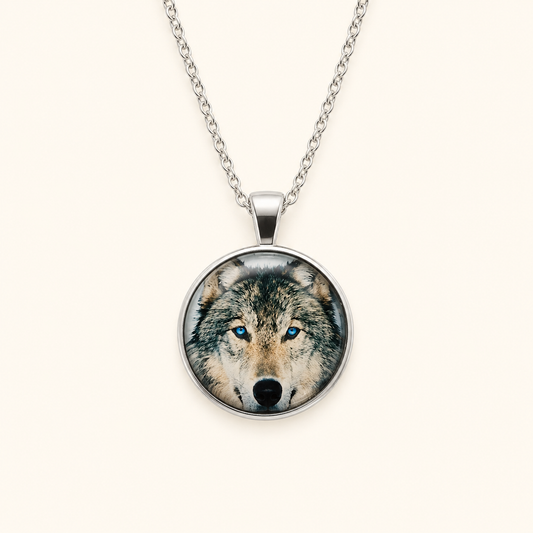 A silver chain necklace with a round pendant featuring a detailed photograph of a wolf's face with bright blue eyes, set against a plain off-white background.
