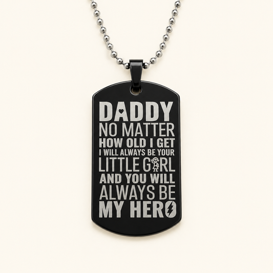 A black dog tag pendant necklace with silver-toned text reading 'DADDY NO MATTER HOW OLD I GET I WILL ALWAYS BE YOUR LITTLE GIRL AND YOU WILL ALWAYS BE MY HERO' on a light cream background.