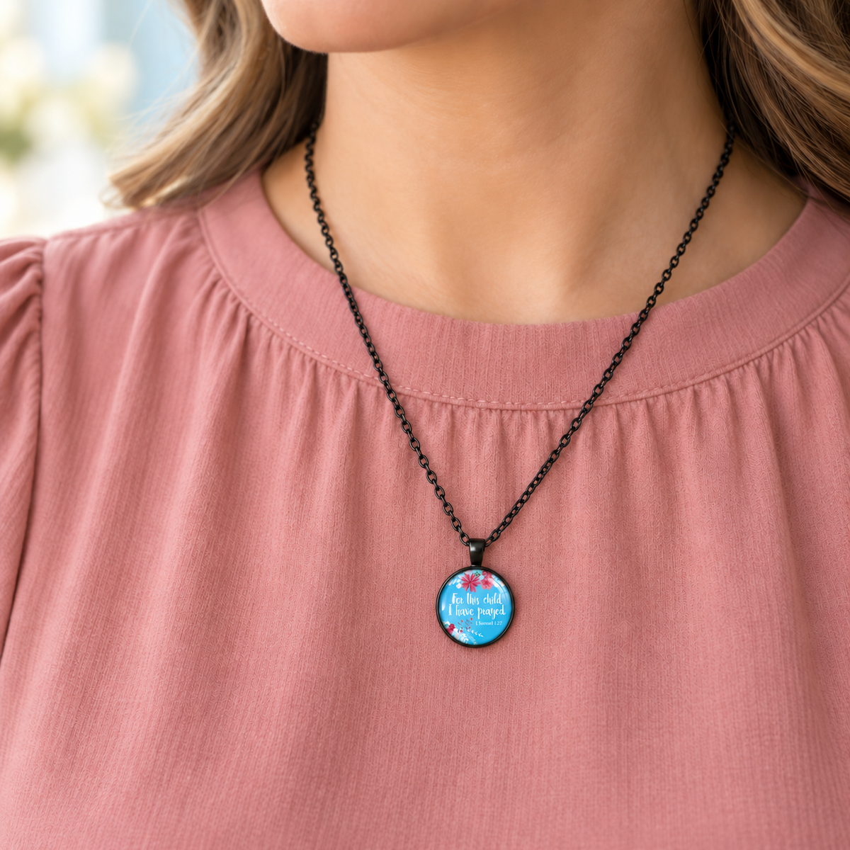 Woman wearing a round black necklace with blue floral artwork and the words “For this child I have prayed” from 1 Samuel 1:27.