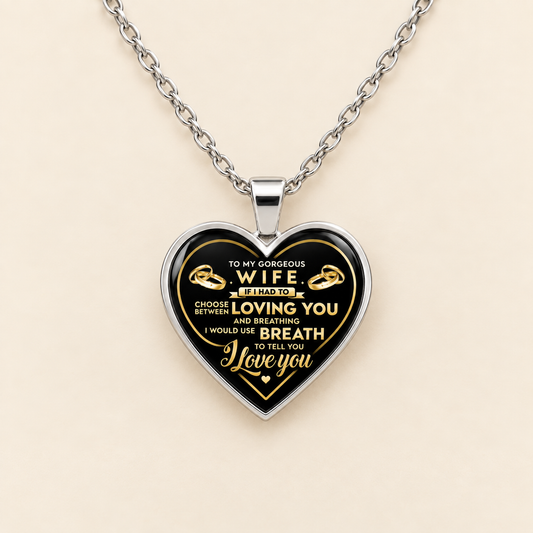 A silver heart-shaped pendant necklace with a black and gold engraved design, reading 'TO MY GORGEOUS WIFE I FIND IT CHOOSING LOVING YOU AND BREATHING I WOULD NOT LET YOU TELL YOU Love you', displayed on a light beige background.