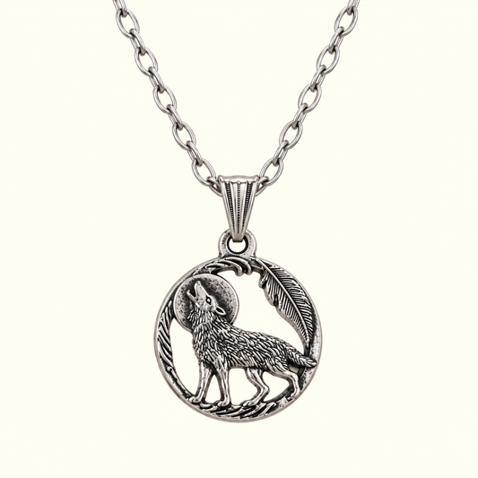 A silver-toned pendant necklace featuring a detailed circular charm with a howling wolf, a feather, and a crescent moon, suspended from a matching link chain against a light cream background.