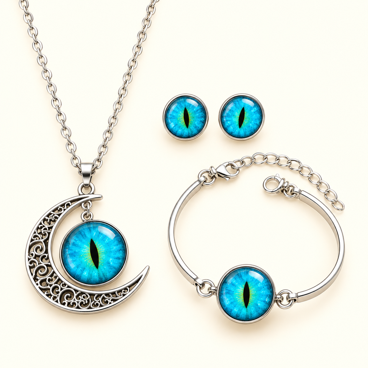 A silver-toned jewelry set featuring a crescent moon pendant necklace, a bangle bracelet, and matching stud earrings, each with a round blue and green eye motif on a light cream background.
