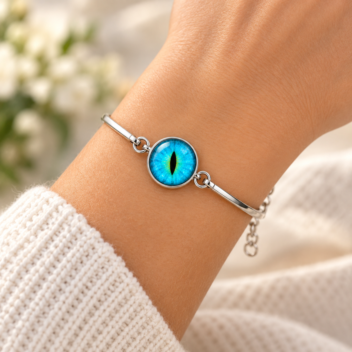 A silver bangle bracelet with a round blue and green eye motif in the center, worn on a person's wrist.