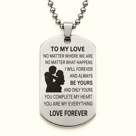 A silver-toned stainless steel dog tag pendant necklace engraved with a romantic message for a partner, featuring a silhouette of a couple and the words 'LOVE FOREVER' at the bottom, shown on a clean off-white background.