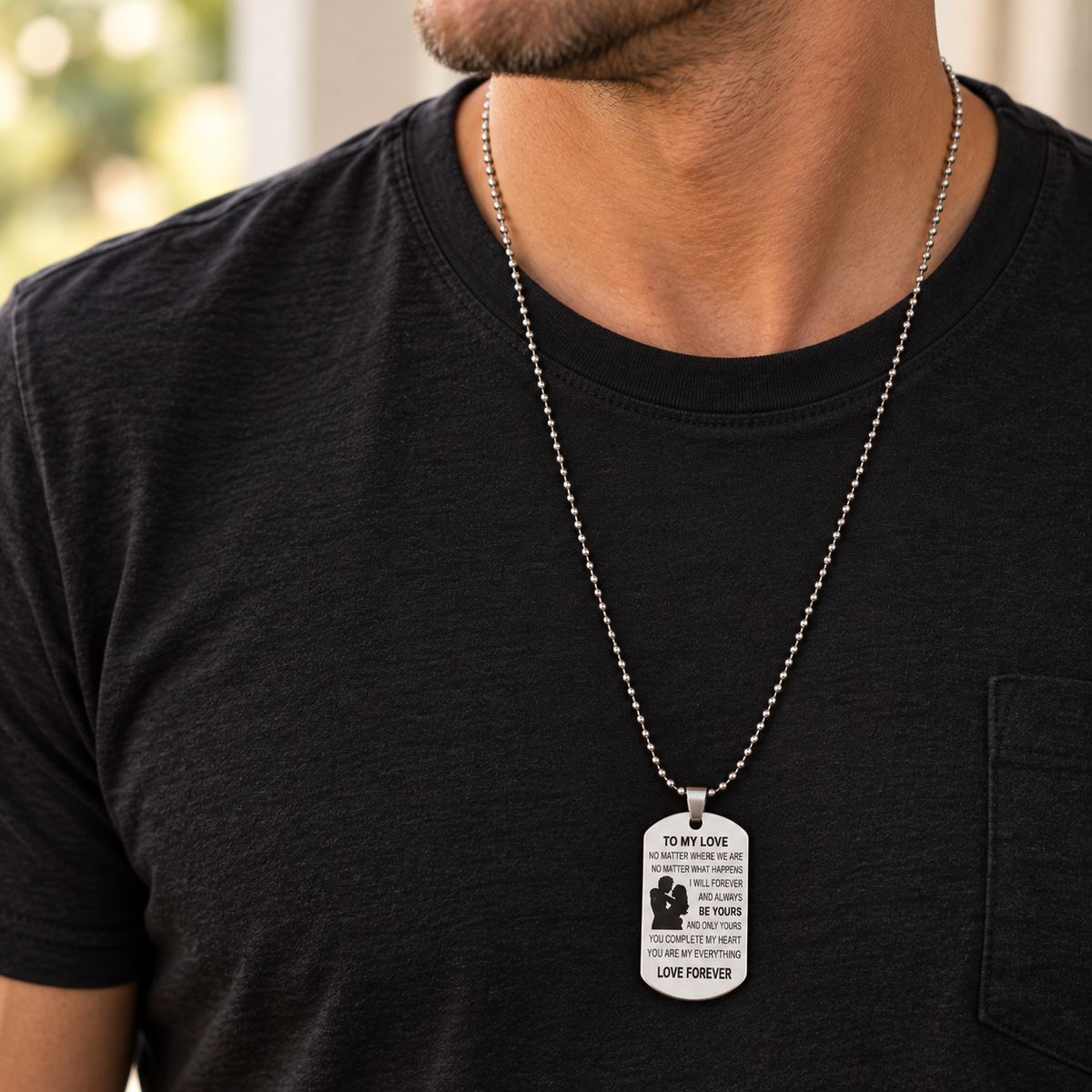 A man wearing a silver ball-chain necklace with a rectangular engraved pendant