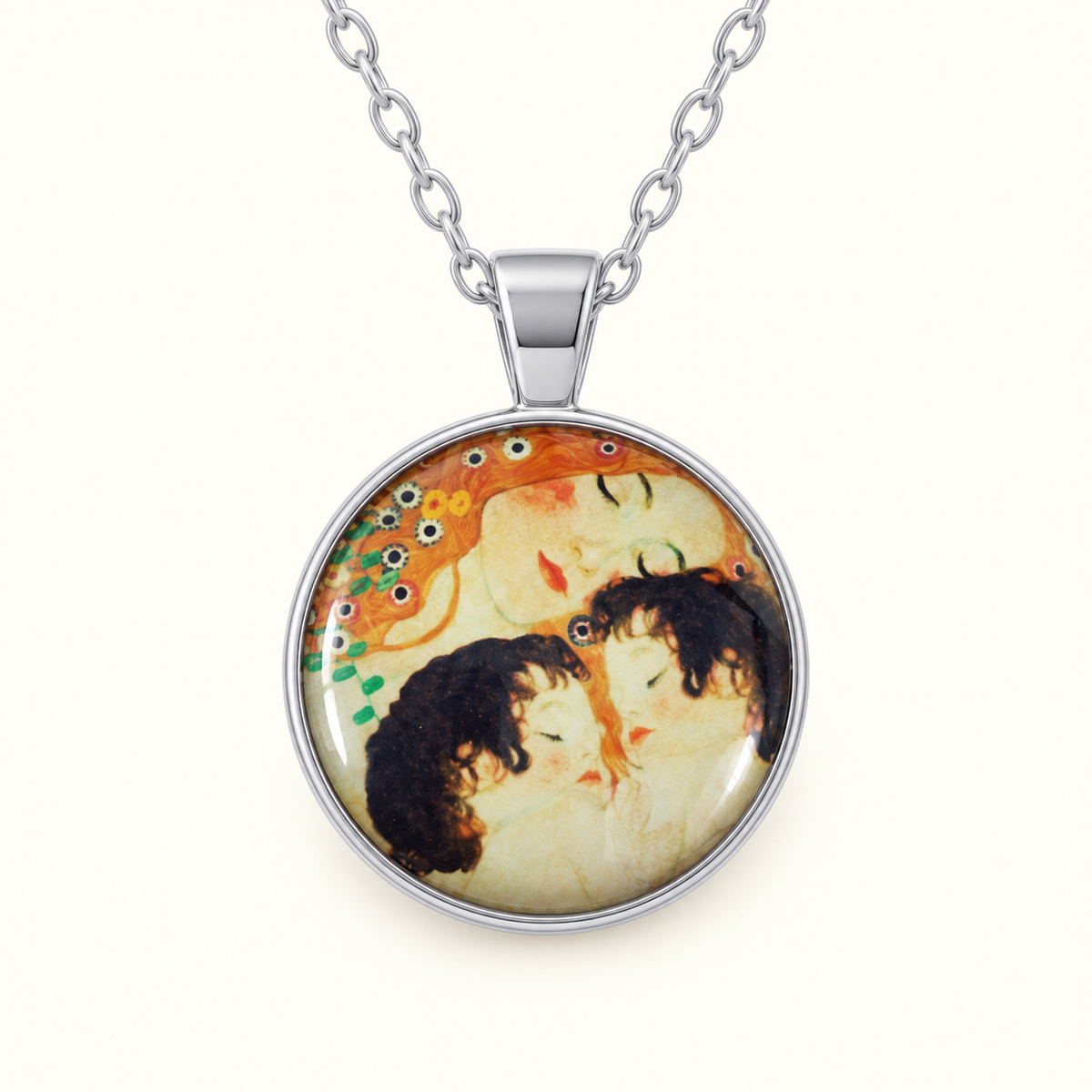 A silver pendant necklace featuring a circular glass cabochon with an art print of two embracing figures, suspended from a silver link chain against a light cream background.