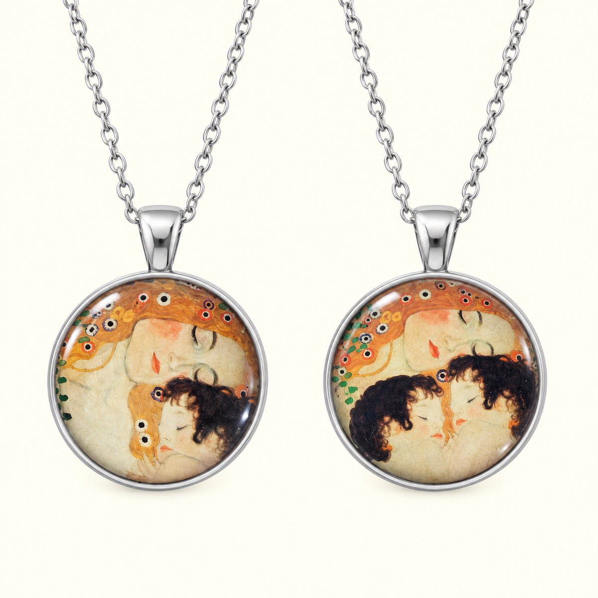 Two matching silver chain necklaces with round pendant frames featuring a vintage-style illustration of two embracing figures in warm beige, orange, and black tones, shown on a light cream background.