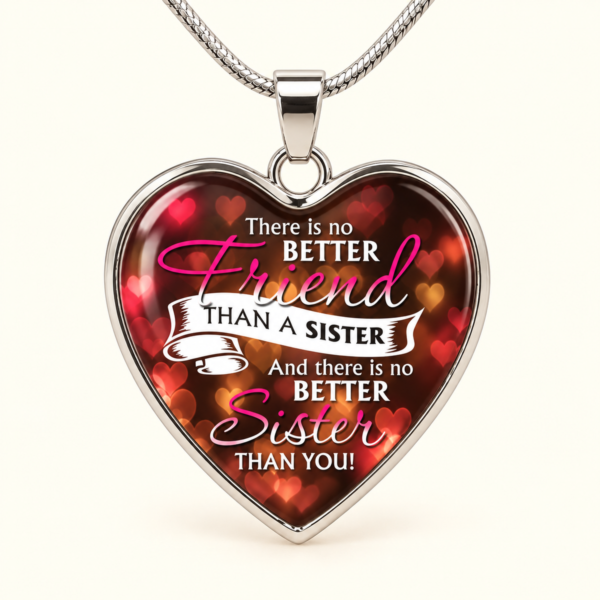 A heart-shaped pendant necklace with a silver-toned metal frame and chain, featuring a printed design with red and pink heart bokeh and the text 'There is no Friend than a Sister And there is no Sister than You!' on a light cream background.