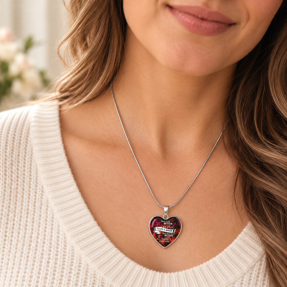 A close-up of a woman wearing a silver chain necklace with a heart-shaped pendant. The pendant features a colorful floral background with a white banner that reads 'I Love You'.
