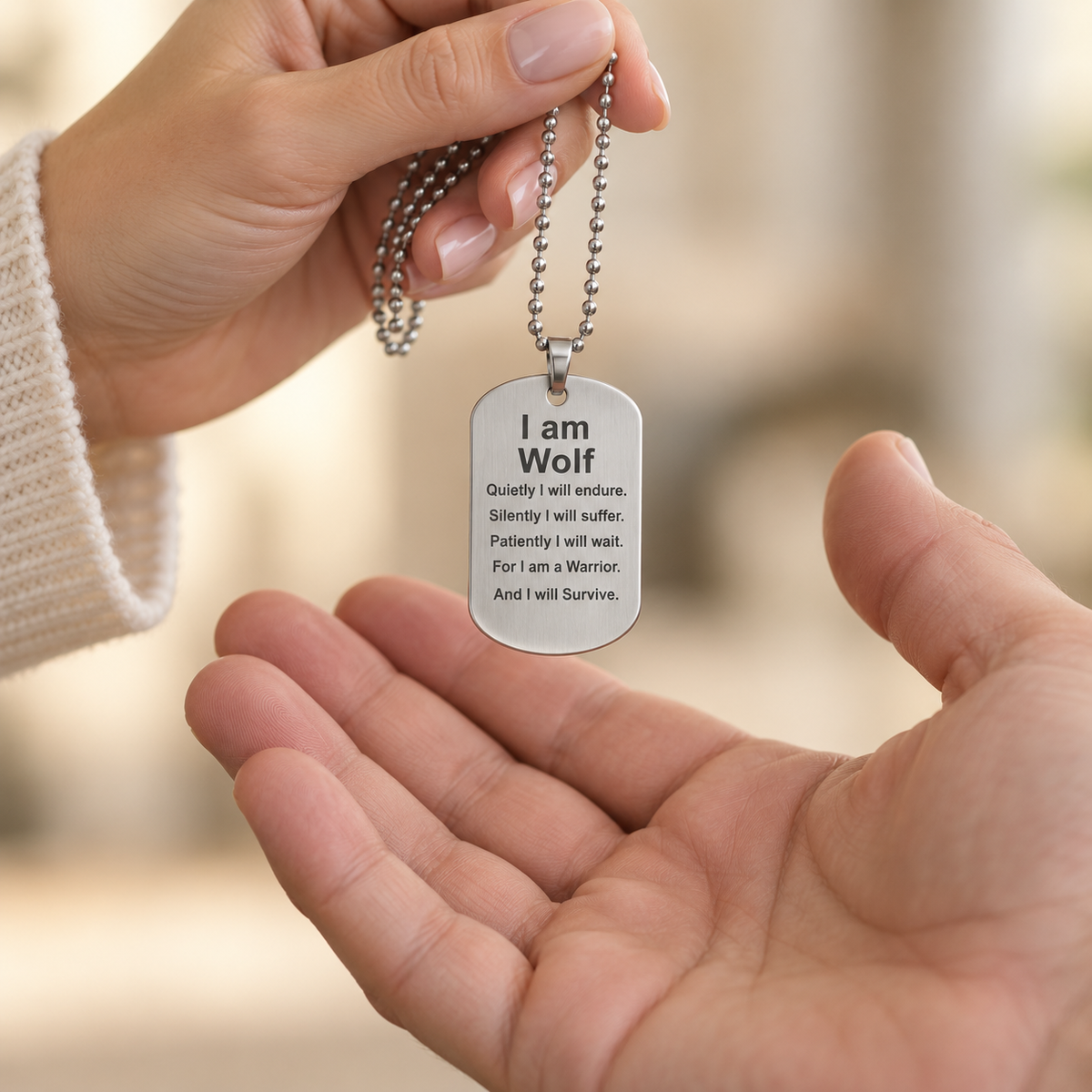 Silver I Am Wolf dog tag necklace being passed between two hands, showing its realistic size and engraved strength message.